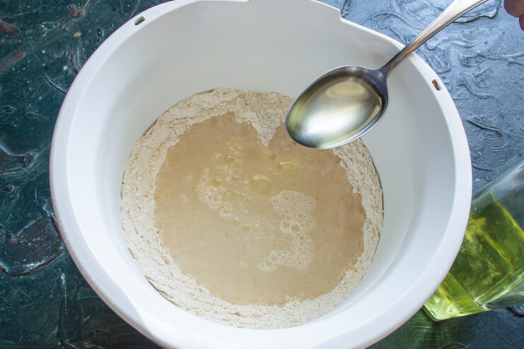 Adding Liquid Ingredients Pouring water and vegetable oil into a mixing bowl containing flour and yeast.