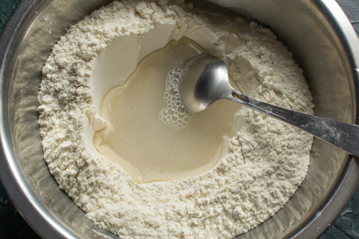 Pouring salted water into a flour well to mix dough