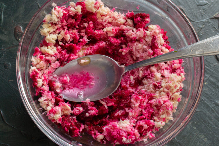 Adding vinegar and sugar Pouring apple cider vinegar into a bowl containing the vibrant horseradish and beet mixture.