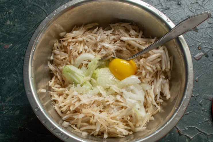 Mixing the base ingredients Adding a cracked egg and diced onion to grated sunchokes