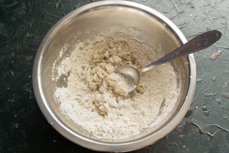 Adding egg and water to flour Adding a cracked egg and cold water into a well in the flour mixture