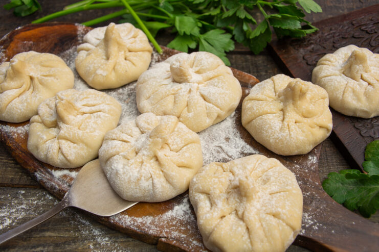 Homemade chicken khinkali served on a wooden board with fresh herbs