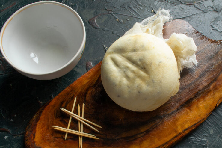 Finished homemade cheese after maturing Finished wheel of homemade cheese on a board next to a bowl