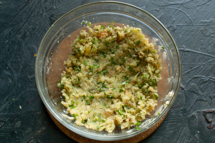 Mixing the filling ingredients thoroughly Fully mixed, sticky filling with herbs, nuts, and cheese in a glass bowl.