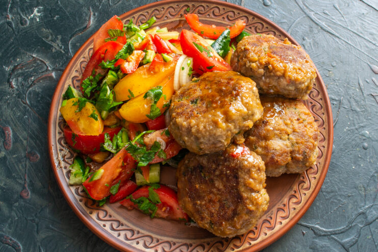 Serving the dish Cooked beef patties with a side of fresh vegetables on a plate