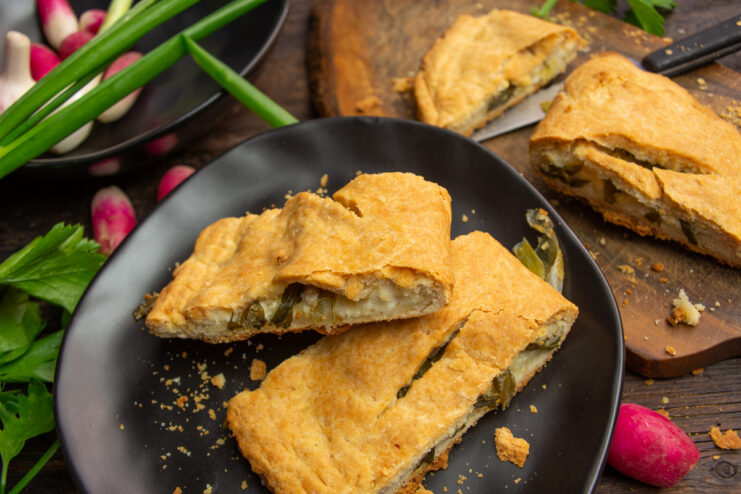Freshly baked pie with cheese, scallions, and farmer's cheese served on a dark plate
