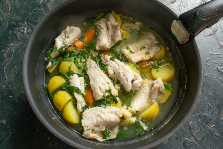 Finished soup in the pot Freshly cooked fish soup with tender white fish pieces and bright spinach in a pot