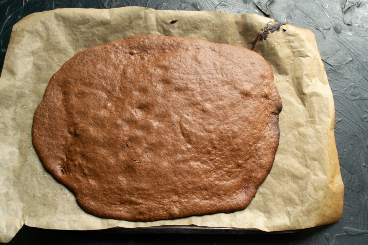 Baked chocolate sponge cake layer on parchment paper.