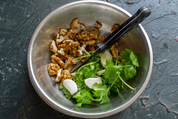 Preparing the sauce ingredients Toasted walnuts, fresh garlic, and cilantro gathered in a metal bowl