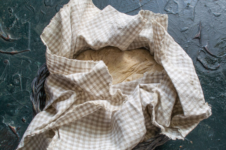 Cold Fermenting The Dough Bread dough resting in a basket covered with a checkered cloth for cold fermentation.