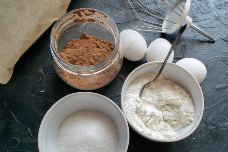 Batter ingredients Eggs sugar flour and cocoa powder on a table