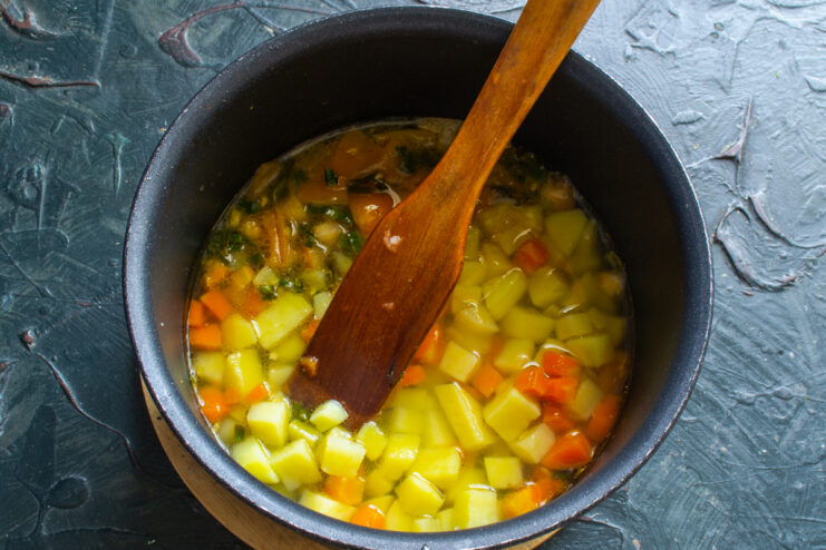 Diced potatoes and carrots simmering in savory broth inside a saucepan