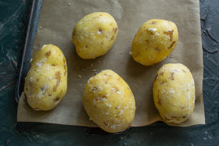 Pre-baking preparation Raw potatoes rubbed with butter and salt on a baking sheet