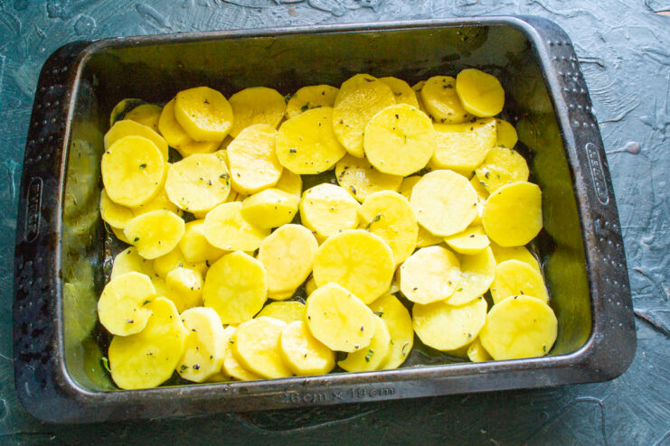 Potato slices tossed with olive oil and thyme in a baking dish