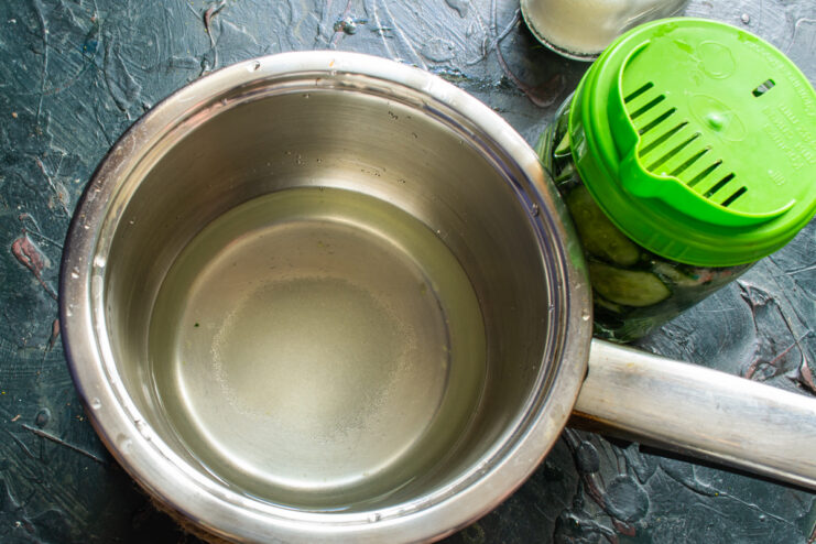 Making the Pickle Marinade Saucepan with boiling marinade next to a glass jar of cucumbers