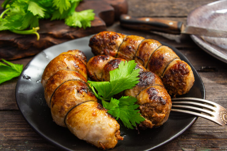 Pan-fried beef sausages with cheese and garlic on a plate with fresh herbs