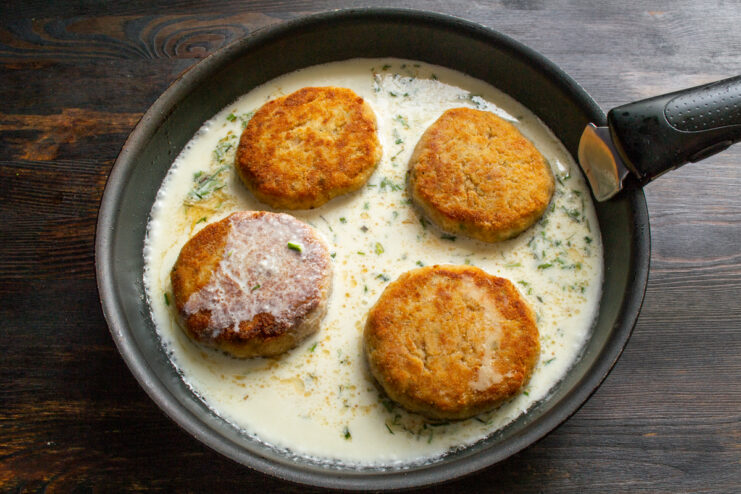 Adding the sauce Fried chicken patties in a skillet covered with a creamy white sauce