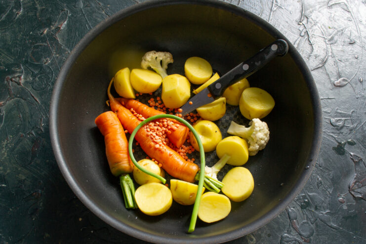 Adding the lentils Red lentils and garlic scapes added to the mixed vegetables in a pot