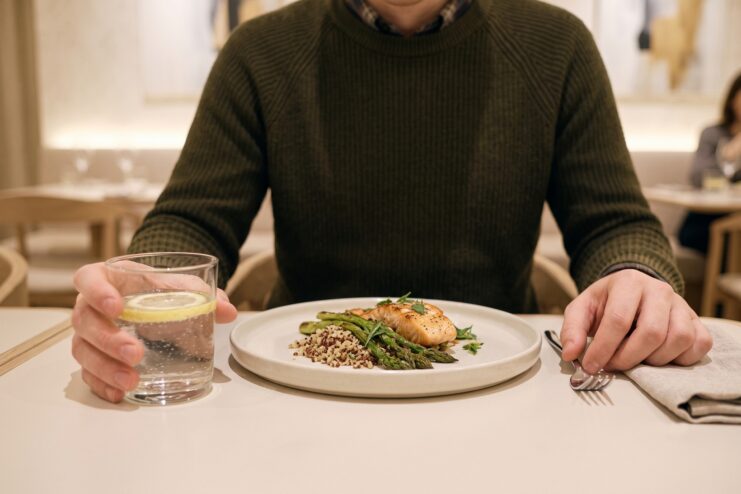 Tension and movement control while eating Close-up of a man's hands at a table with a plate of fish and a glass of lemon water.