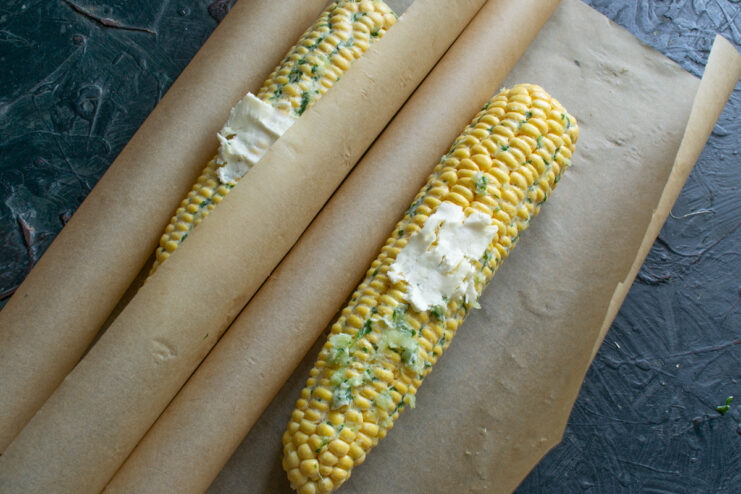 Prepping for parchment baking Corn on parchment paper topped with extra butter pats
