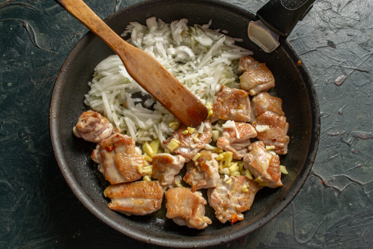 Cooking chicken with diced onion, garlic, and fresh ginger in a skillet