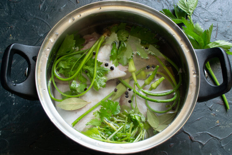Boiling the chicken broth Chicken simmering in a pot with fresh herbs and spices
