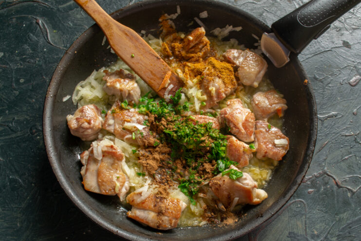 Seasoning chicken with curry powder, paprika, and fresh herbs in a pan