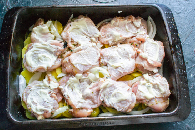 Raw chicken thighs coated with sour cream in a baking dish