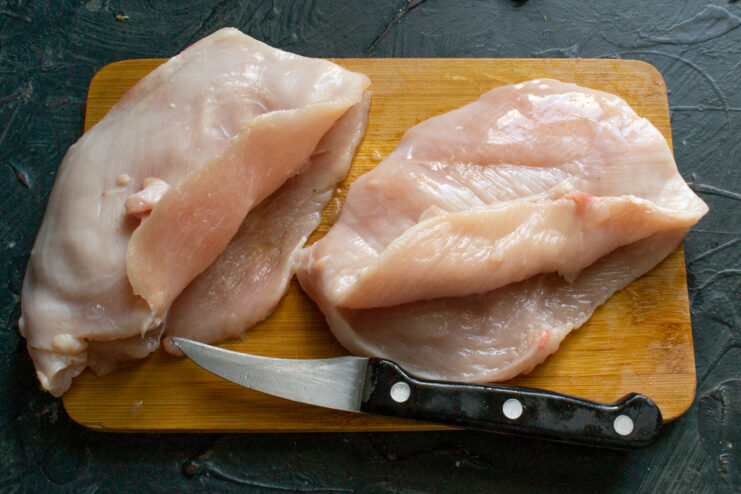 Cutting a pocket into the chicken fillet A sharp knife cutting a deep pocket into the thick part of a raw chicken breast fillet.