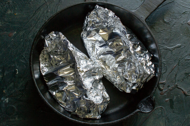 Crimping the foil edges for baking Foil edges tightly crimped into a boat shape to seal the chicken and retain juices during baking.