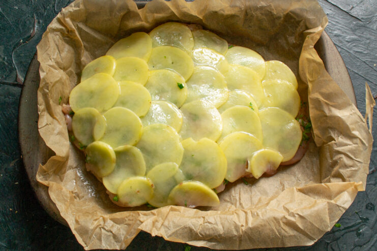 Raw chicken fillet fully covered by overlapping scalloped potato slices