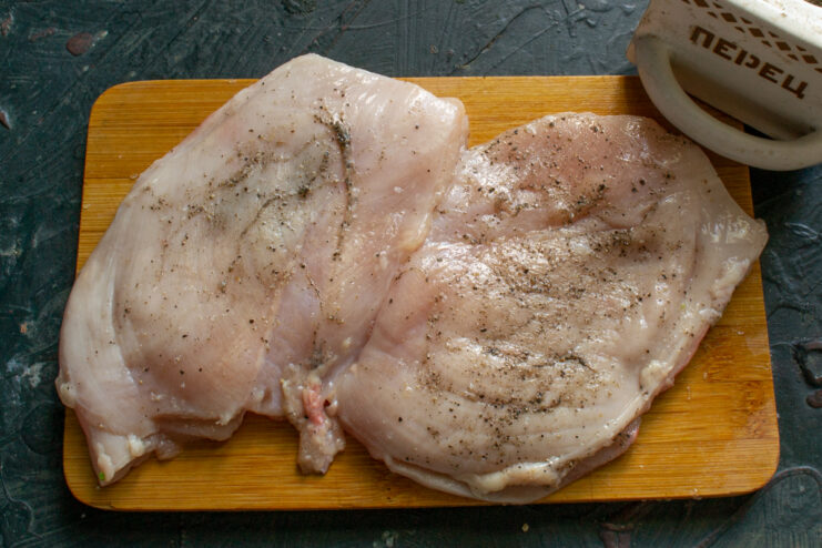 Seasoning the chicken breast inside and out Raw chicken breast seasoned evenly with salt and black pepper, inside the pocket and out.