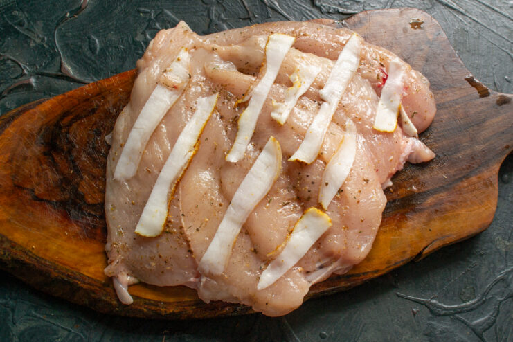 Raw chicken breast topped with thin strips of pork fat
