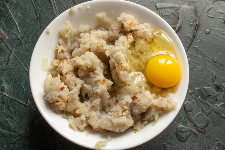 Adding the Binding Ingredient A raw chicken egg added to a mixing bowl with minced fish.