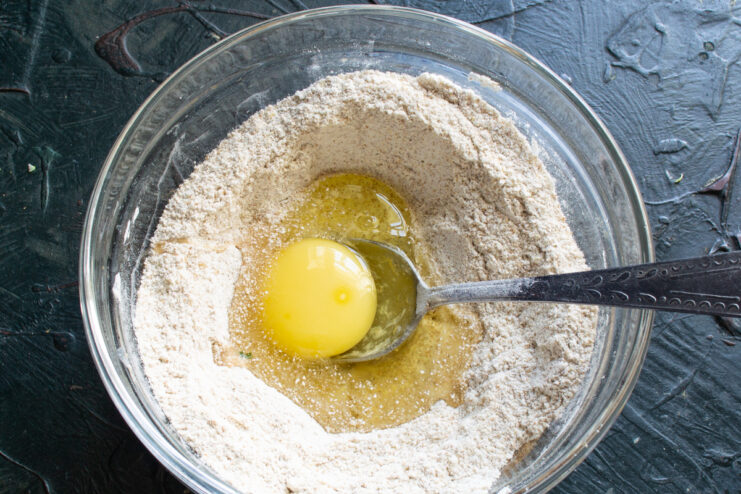Adding the liquid ingredients A cracked egg and neutral oil sitting in the center of the flour mixture