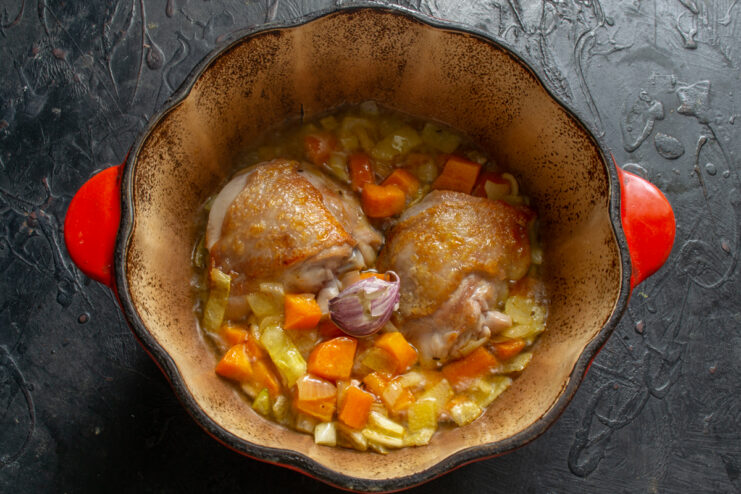 Chicken with vegetables and garlic Chicken thighs and whole garlic clove in a Dutch oven with vegetables