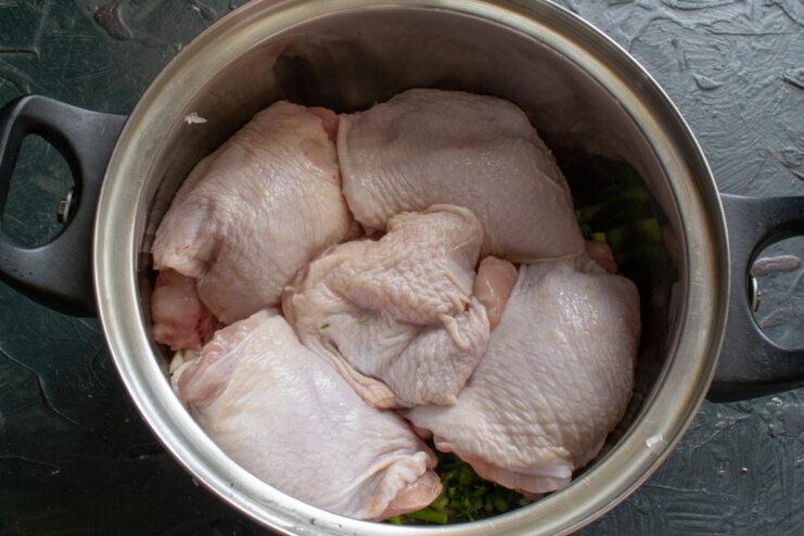 Adding chicken to the pot Raw chicken thighs in a pot with onions and herbs.