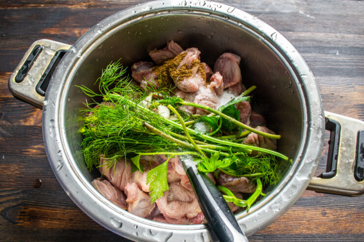 Adding herbs and spices Chicken gizzards in a pot with fresh herbs and spices