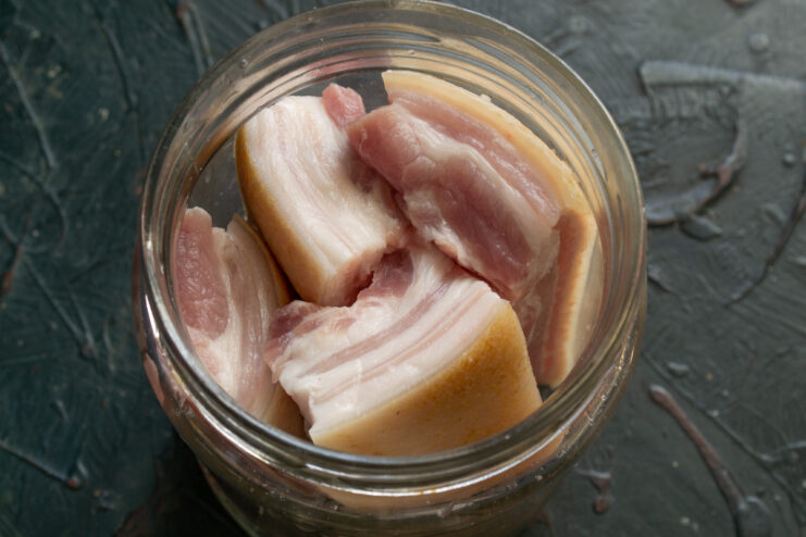 Preparing for the Wet Cure Pieces of raw pork belly packed in a glass jar before adding the brine