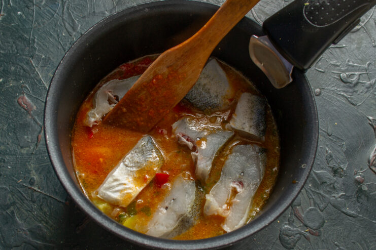 Raw white fish pieces being gently added to a pot with a simmering vegetable base.