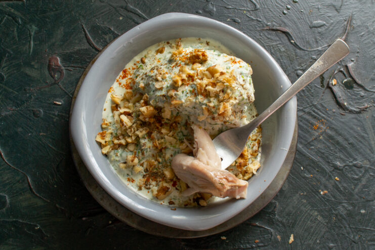 Serving the chicken with sour cream A piece of chicken on a fork coated in white sauce with walnuts.