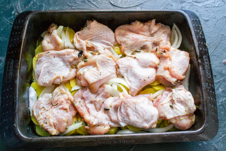 Placing marinated chicken thighs over the layer of onions and potatoes