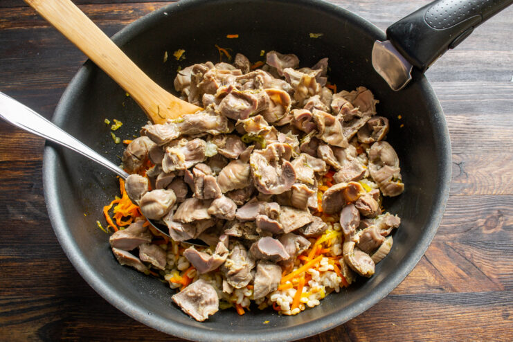 Combining the ingredients Adding chopped chicken gizzards to the pearl barley and vegetables