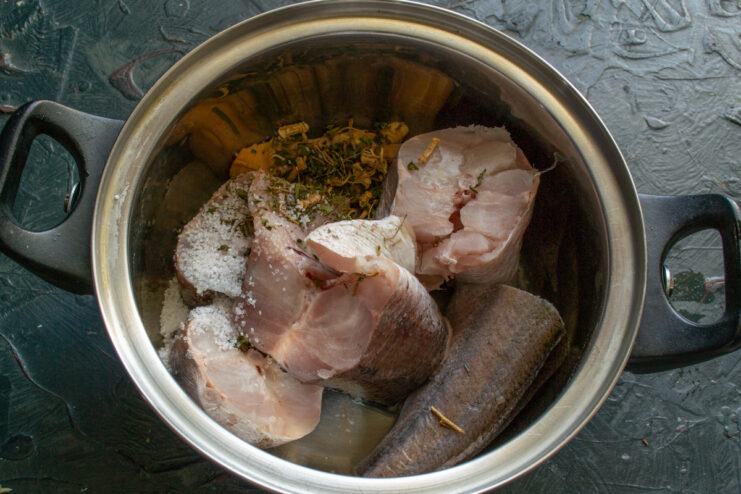 Seasoning the Broth Fish pieces inside a cooking pot with salt and dried herbs.