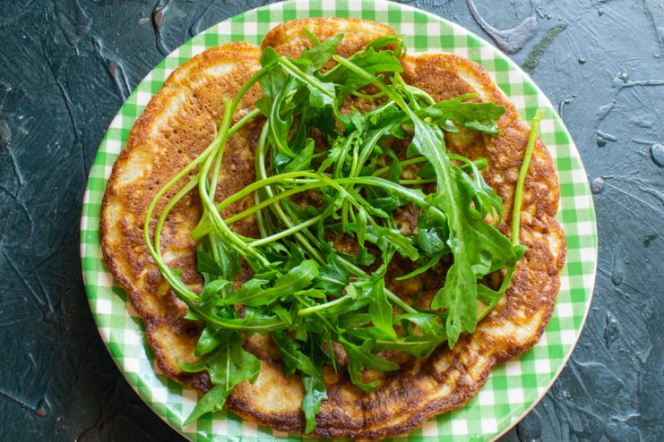 Layering the arugula Fresh arugula leaves spread evenly over a cooked oatmeal pancake