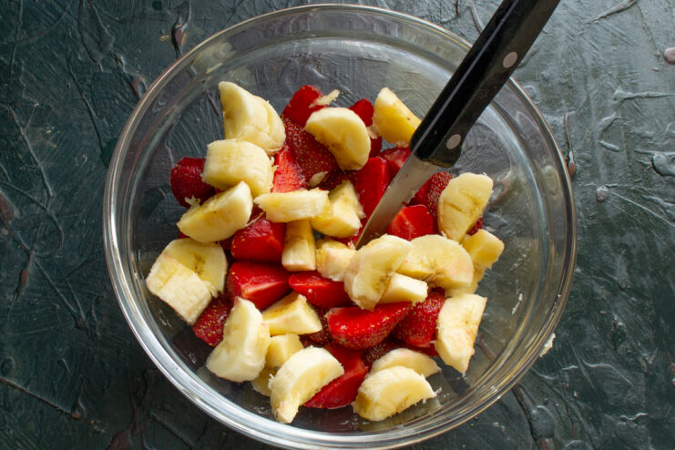 Adding Banana Slices Banana slices added to the glass bowl with strawberries