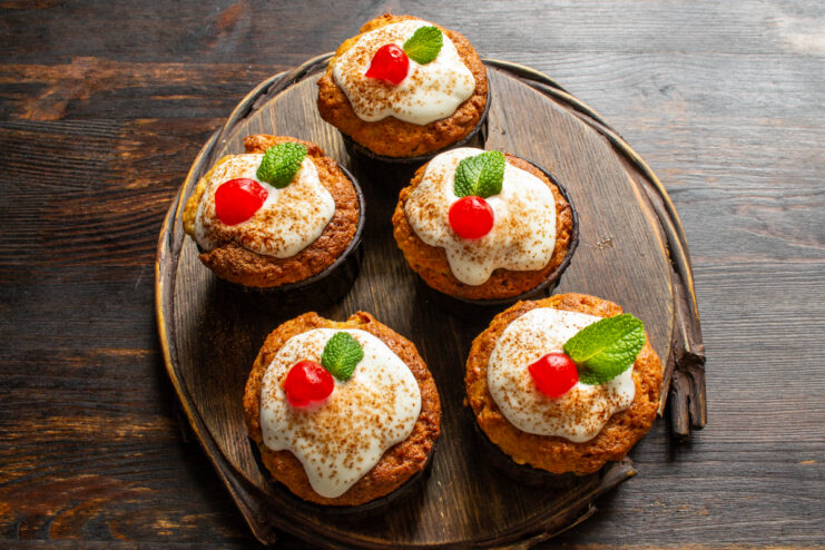 Garnishing with frosting and berries Decorated muffins topped with white frosting, cocoa powder, and fresh mint on a wooden board.