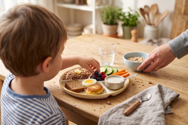 Toddler eating buckwheat, egg, berries, and vegetables from a sectioned plate