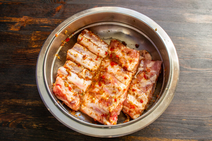 Marinating the pork ribs Pork ribs marinated in adjika and oil inside a metal mixing bowl.