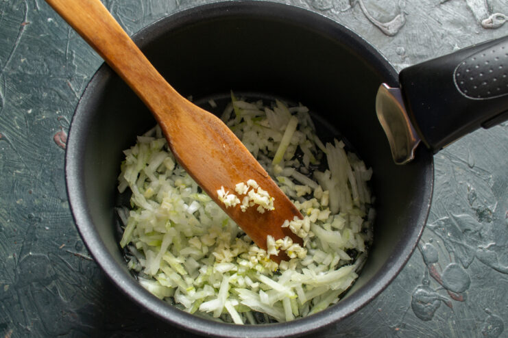 Finely chopped onion and minced garlic sauteing in hot oil at the bottom of a pot.